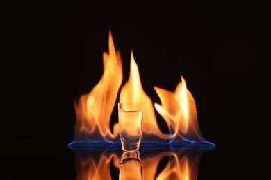 Photo of Vodka in shot glass and flame on black background