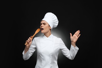 Photo of Emotional female chef singing with wooden spoon on black background