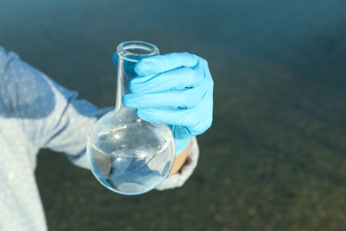 Scientist with florence flask taking sample from river for analysis, closeup