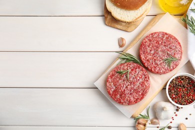Raw hamburger patties with rosemary and pepper on white wooden table, flat lay. Space for text