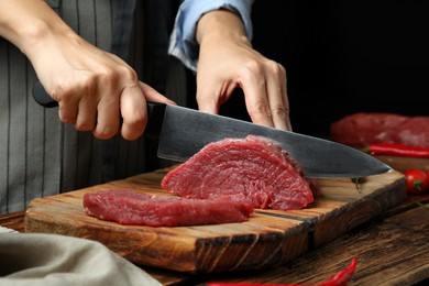 Woman cutting fresh raw meat at wooden table, closeup