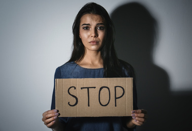 Abused young woman with sign STOP near white wall. Domestic violence concept