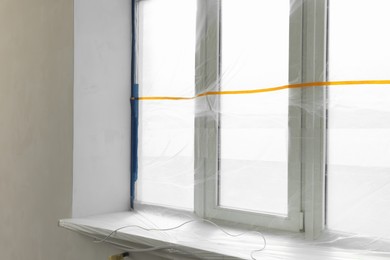 Window covered by plastic film and insulation tape indoors
