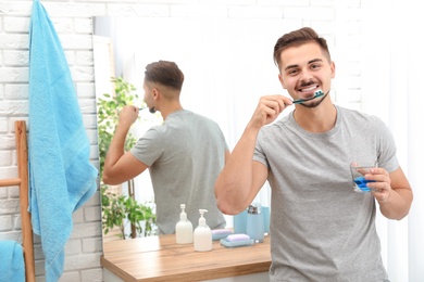 Young man brushing teeth in bathroom at home. Space for text