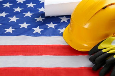 Yellow protective hard hat, gloves and construction drawing on American flag. Space for text