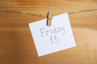 Paper note with phrase Friday 13 hanging on twine against wooden background. Bad luck superstition