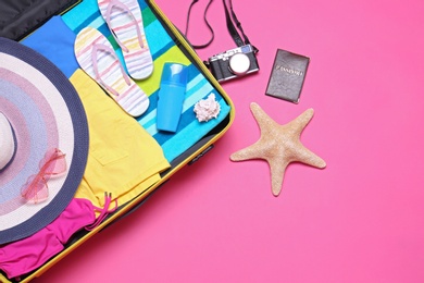 Open suitcase and beach objects on pink background, flat lay