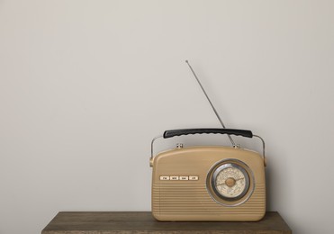 Retro radio receiver on wooden table against light grey background. Space for text