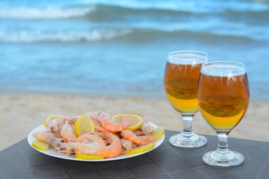 Photo of Cold beer in glasses and shrimps served with lemon on beach