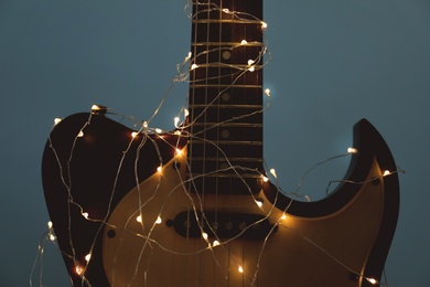 Guitar with glowing fairy lights on dark background, closeup. Christmas music