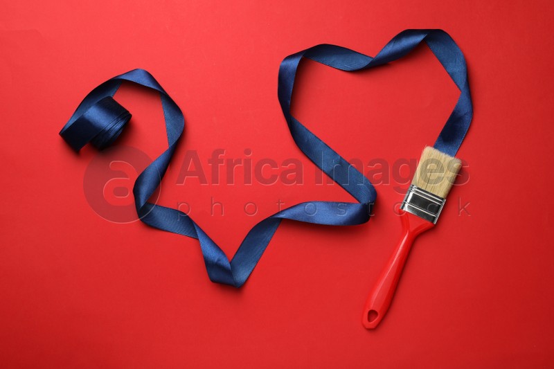 Brush painting with dark blue ribbon on red background, flat lay. Creative concept