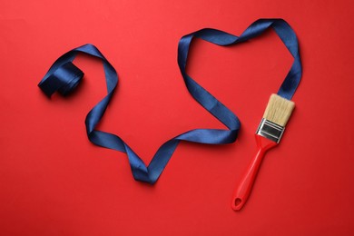 Photo of Brush painting with dark blue ribbon on red background, flat lay. Creative concept
