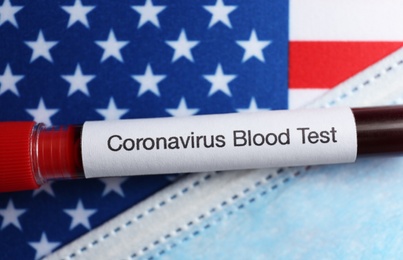 Test tube with blood sample and medical mask on American flag, flat lay. Coronavirus pandemic in USA