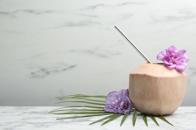 Young peeled coconut with straw, palm leaf and flowers on white marble table. Space for text