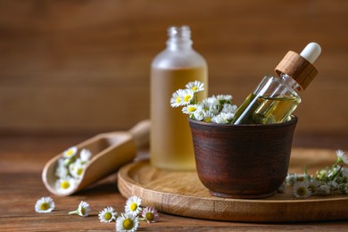 Chamomile essential oil and flowers on wooden table, space for text