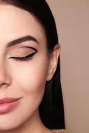 Photo of Beautiful woman with black eyeliner on beige background, closeup