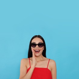 Attractive happy woman in fashionable sunglasses against light blue background
