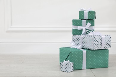 Many gift boxes on wooden floor near white wall. Space for text