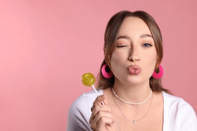 Young woman with lip and ear piercings holding lollipop on pink background, space for text