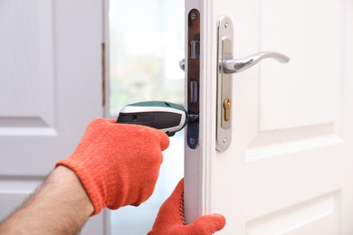 Handyman with screw gun repairing door lock indoors, closeup