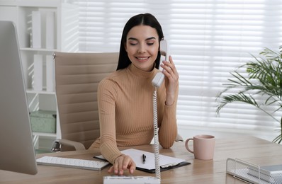 Secretary talking on phone at wooden table in office