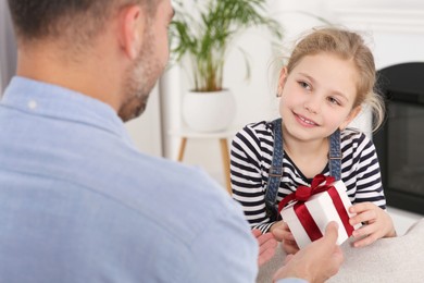 Photo of Cute little girl presenting her father with gift at home