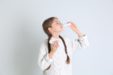 Sick little girl using nasal spray on white background