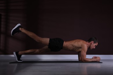Handsome man doing plank exercise with leg lift on floor indoors