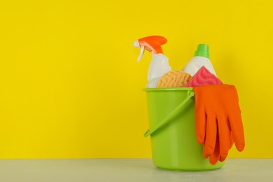 Bucket with different cleaning supplies on light floor near yellow wall. Space for text
