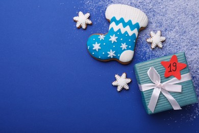 Gift box with paper tag, gingerbread cookies and space for text on blue background, flat lay. December, 19 - Saint Nicholas Day
