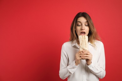 Photo of Emotional young woman with delicious shawarma on red background, space for text