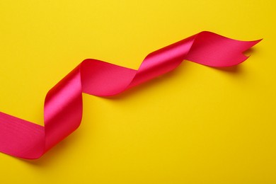Beautiful pink ribbon on yellow background, top view. Space for text