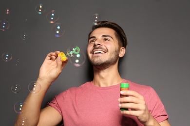 Photo of Young man blowing soap bubbles on color background