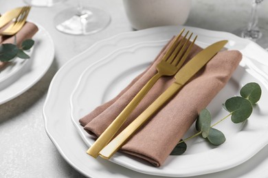 Photo of Stylish setting with cutlery and eucalyptus leaves on light grey table, closeup