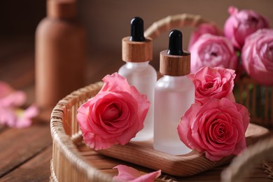 Tray with bottles of essential rose oil and flowers on wooden table, closeup