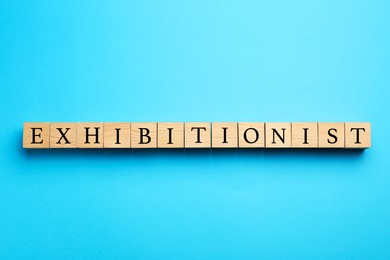 Word EXHIBITIONIST made with wooden cubes on light blue background, flat lay
