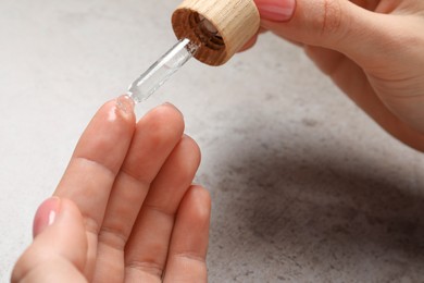 Woman dripping serum from pipette on her hand at grey table, closeup