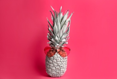 Photo of Painted pineapple with heart shaped sunglasses on pink background. Creative concept