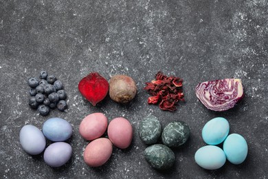 Photo of Painted Easter eggs with natural organic dyes (blueberries, beetroot, hibiscus, and red cabbage) on black table, flat lay. Space for text