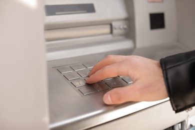 Photo of Man entering PIN code on cash machine keypad outdoors, closeup view
