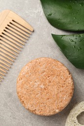 Solid shampoo bar, monstera leaf and comb on grey table, flat lay