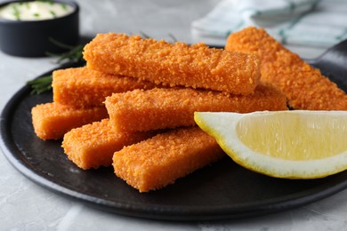 Fresh breaded fish fingers and lemon served on light grey table, closeup