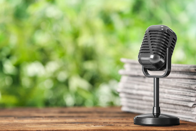 Newspapers and vintage microphone on wooden table against blurred green background, space for text. Journalist's work