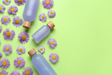 Flat lay composition with bottles of essential oil and daisy flowers on light green background. Space for text