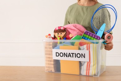Woman holding donation box with child goods against light background, closeup. Space for text