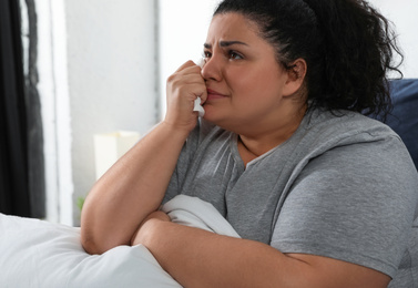 Depressed overweight woman crying while hugging pillow on bed