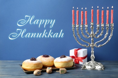 Happy Hanukkah. Silver menorah, dreidels, gift box and sufganiyot on blue wooden table