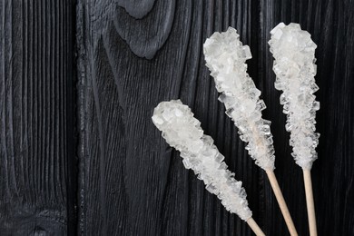 Photo of Sticks with sugar crystals on black wooden table, flat lay and space for text. Tasty rock candies