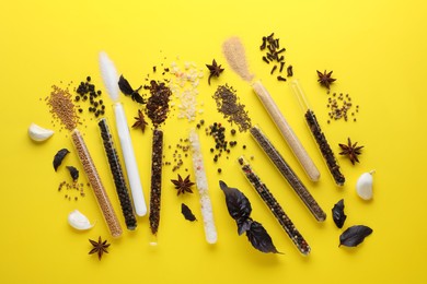 Glass tubes with different spices on yellow background, flat lay