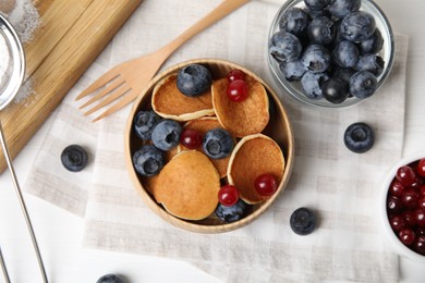 Delicious mini pancakes cereal with berries served on white table, flat lay